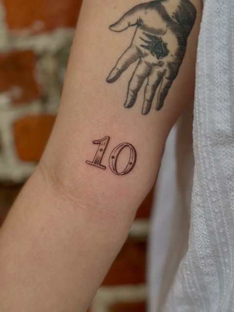 Fine line number ten tattoo with small star details on an arm