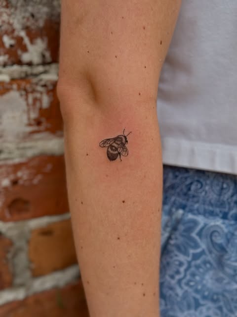 Small black and grey fine line bee tattoo on an arm