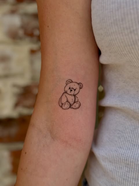 Small fine line teddy bear tattoo on an upper arm